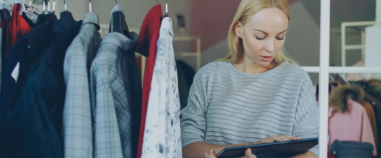 A clothing store owner checking stock on the rails with a tablet