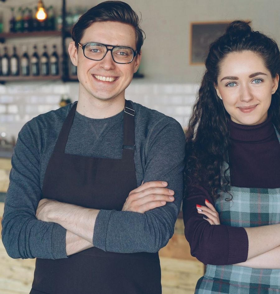 Two young cafe owners standing together inside their coffee shop, smiling