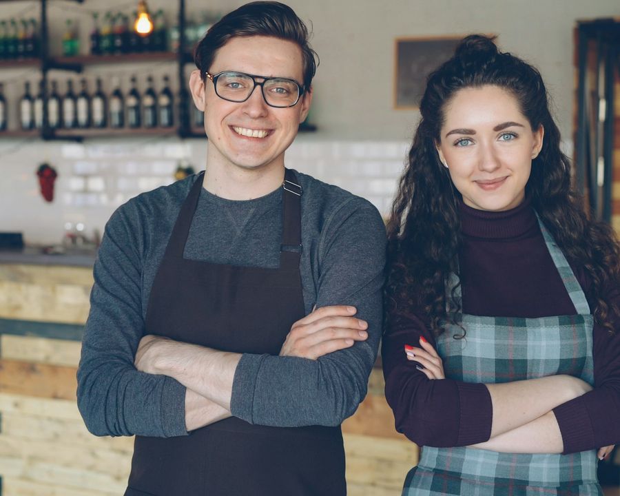 Two young cafe owners standing together inside their coffee shop, smiling