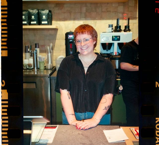 A smiling coffee shop owner standing behind the counter of her cafe