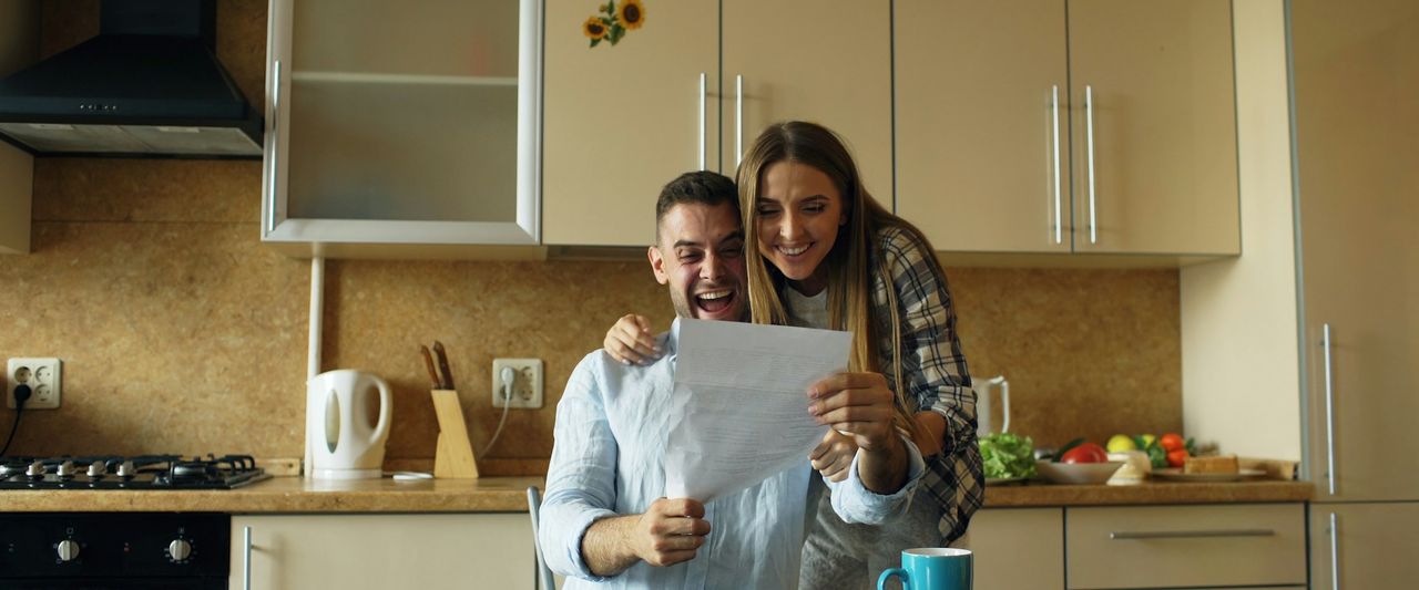 A couple at their kitchen table smiling as they read a letter together