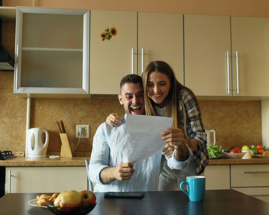 A couple at their kitchen table smiling as they read a letter together