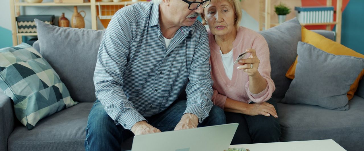 An older couple paying their bills online together on a laptop at home